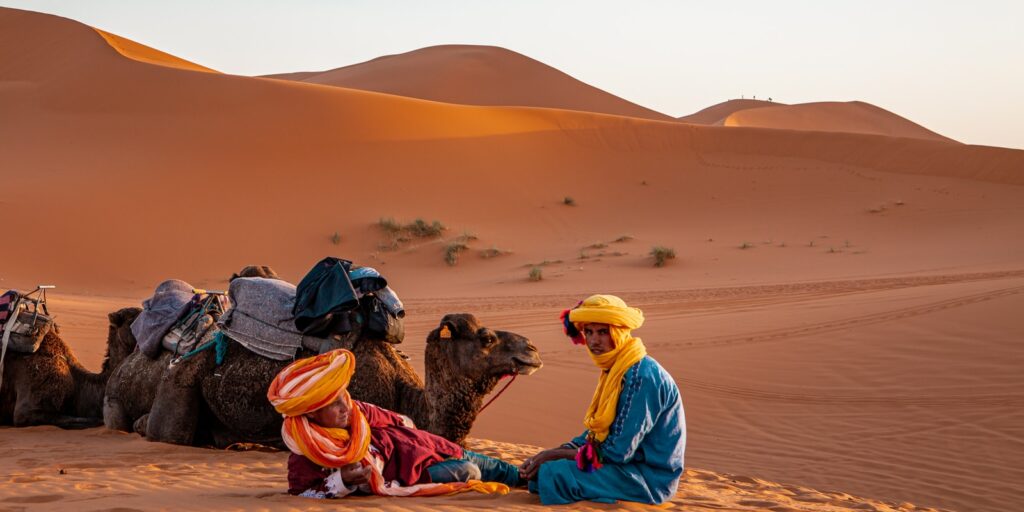 man in yellow robe sitting on brown sand during daytime